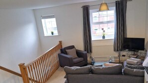 A living room with a grey sofa, a TV, and a staircase. - HEREFORD – Robin Coach House: Modern 2-Bed with Parking on City Outskirts (Hereford)