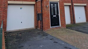 A two-story brick building with a black front door, two garage doors, and a satellite dish. - HEREFORD – Robin Coach House: Modern 2-Bed with Parking on City Outskirts (Hereford)