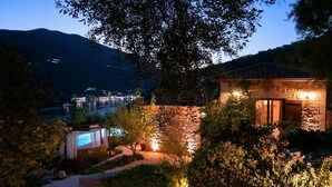 En villa med en swimmingpool, stenmurar och utsikt över en sjö och stadens ljus under skymningen.