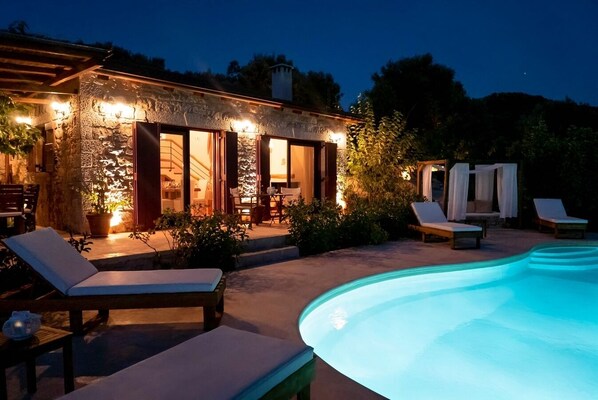 A stone house with a pool, outdoor seating, and a well-lit patio area.