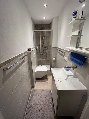 Ein schmales Badezimmer mit Toilette, Dusche und Waschbecken.