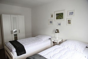A bedroom with two beds, a wardrobe, a nightstand with a lamp, and framed pictures on the wall. - Alpine paradise apartment with balcony and view (Reit im Winkl)