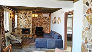 A cozy living room with a stone wall, a fireplace, a sofa, and a television.