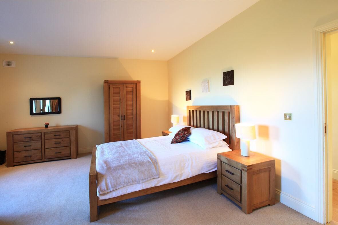 Un dormitorio con cama, mesitas de noche de madera, un armario y un espejo en la pared.