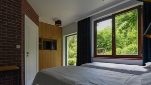 Ein Schlafzimmer mit zwei Betten, einer Ziegelwand, einem Holzschrank und einem Fenster mit Blick auf Grünflächen.
