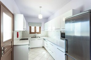Una cocina moderna con armarios blancos, un refrigerador de acero inoxidable y una ventana con persianas.