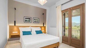 A bedroom with a wooden bed, white bedding, two framed pictures on the wall, a nightstand, and a view of the outdoors through a door.