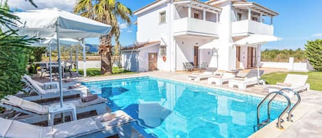 A two-story house with a swimming pool, sun loungers, and a covered patio area.