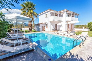 Una casa de dos pisos con piscina, sillas de descanso y un patio cubierto.