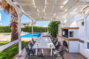 Een terras buiten met een zwembad, lounge stoelen en een barbecueplaats.