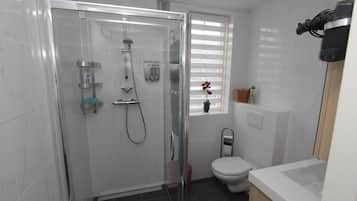 Un baño moderno con ducha de mampara de vidrio, inodoro y lavamanos.
