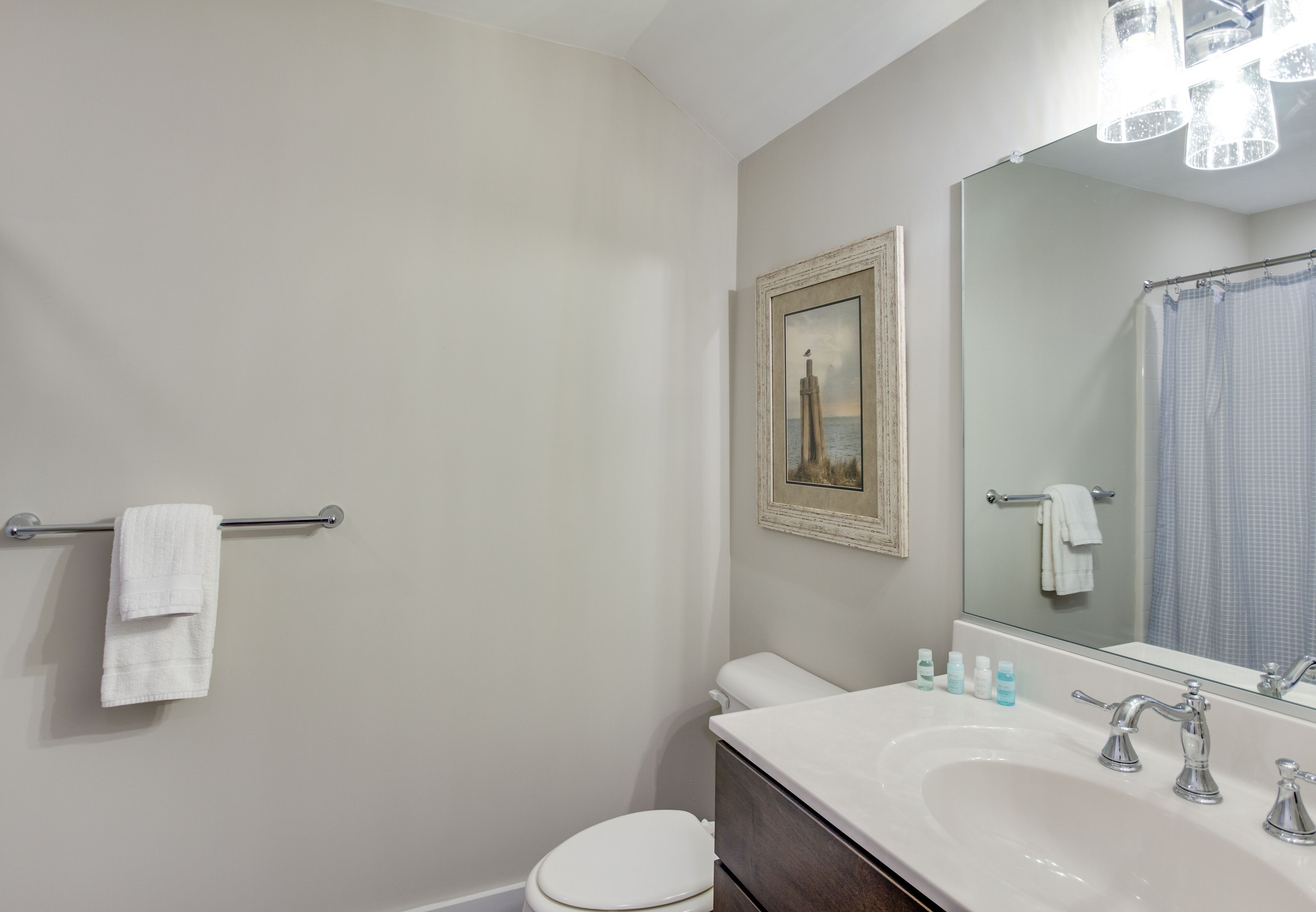 A bathroom with a white toilet, a sink with two faucets, a mirror, and a towel rack.