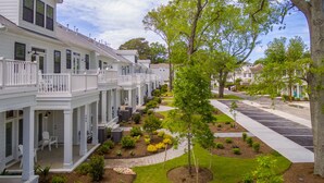 A row of white two-story houses with balconies, a well-maintained lawn, and a tree in the center.