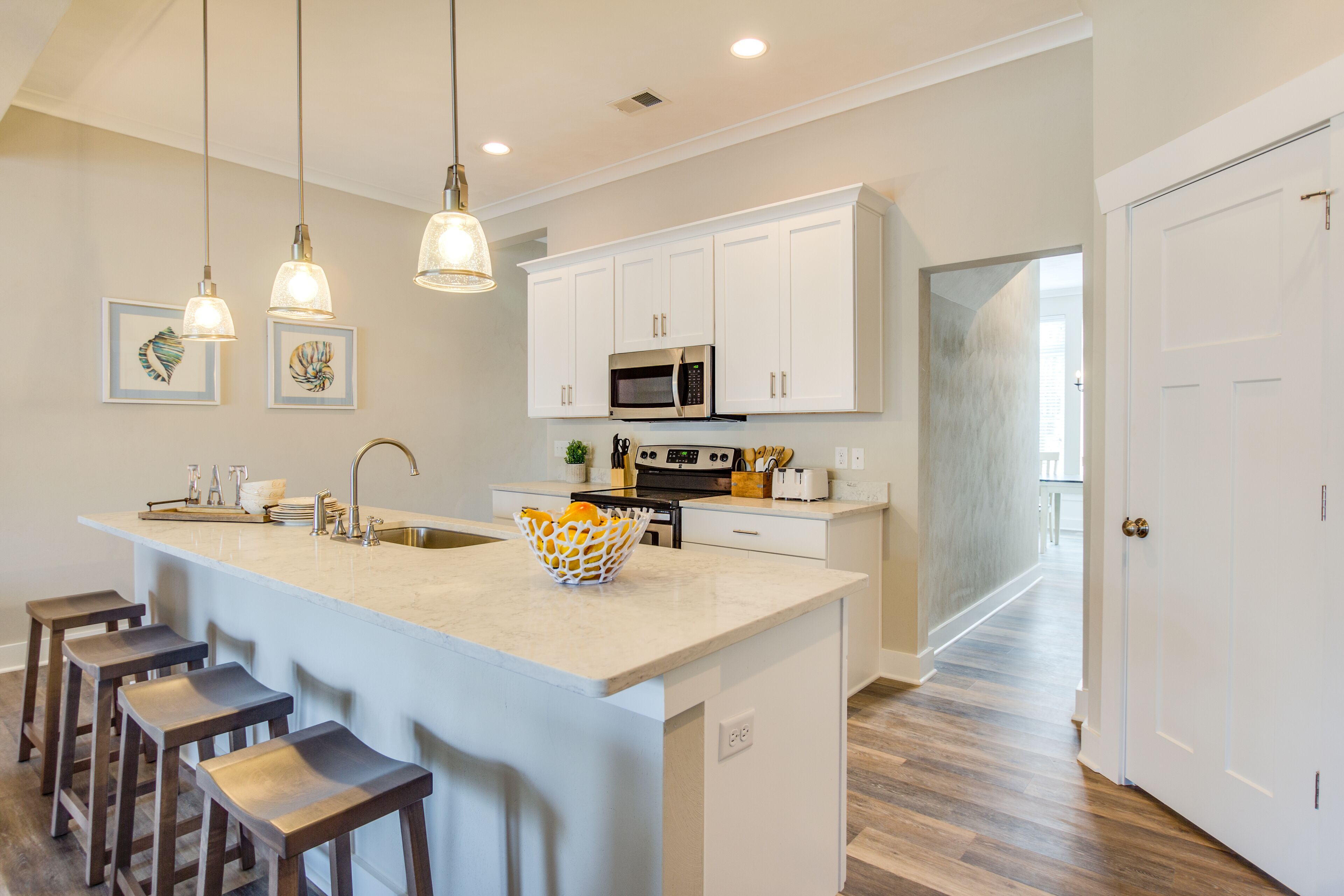 A kitchen with white cabinets, a central island with stools, a microwave, and pendant lighting.
