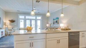 A modern kitchen with white cabinetry, a central island, pendant lighting, and a view of the outdoors through large windows.