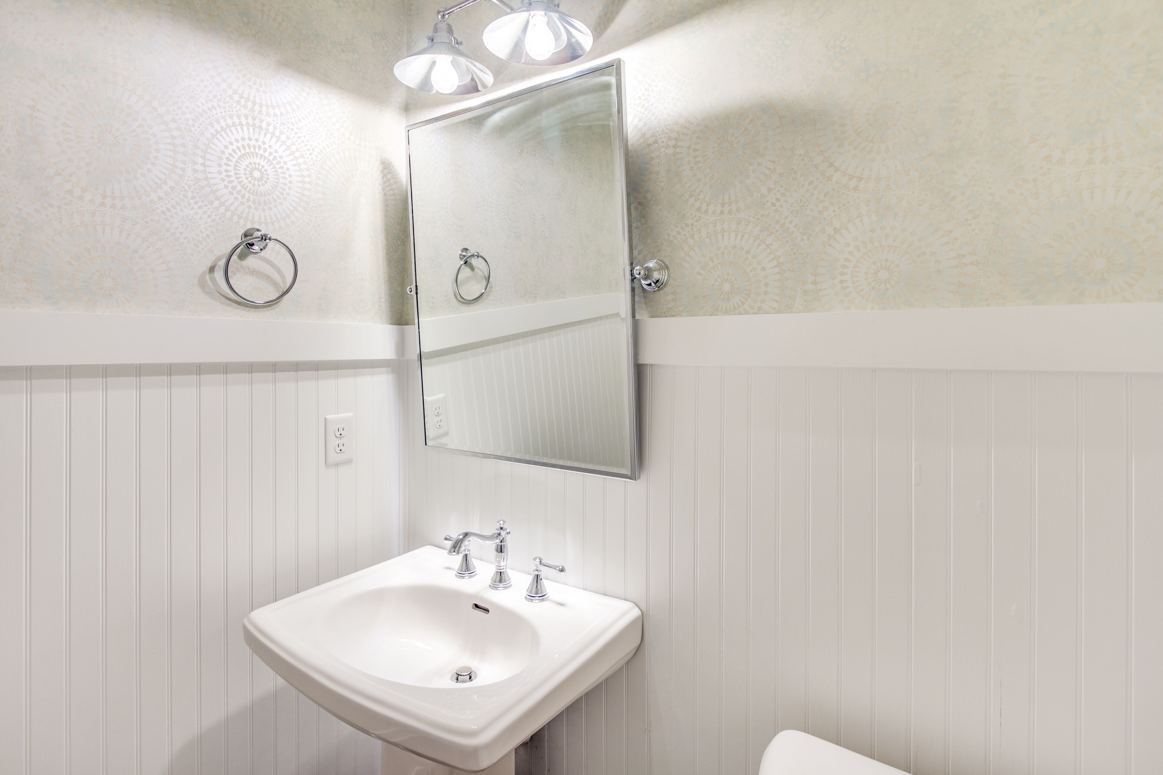 Un baño con lavamanos blanco, un espejo y un perchero para toallas.