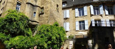 A historic stone building with multiple windows and balconies, surrounded by greenery.