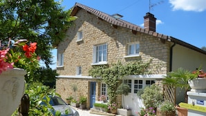 Un bâtiment en pierre avec une voiture garée devant, entouré de plantes et de fleurs en pot.
