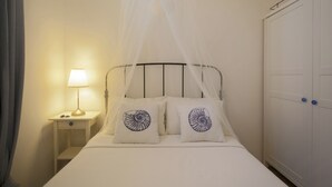 Una cama con dosel, dos almohadas con diseño de caracola, una lámpara de noche, una mesita de noche y un armario.