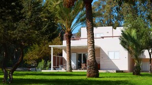 A modern two-story house with a covered patio, surrounded by lush greenery and palm trees. - Ktima Grammeno Villa (Gialos)
