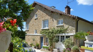 Un bâtiment en pierre avec une voiture garée devant, entouré de plantes et de fleurs en pot.