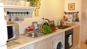 Une cuisine compacte équipée d’un lave-linge, d’un évier et d’un four à micro-ondes. On y trouve divers ustensiles de cuisine et quelques objets décoratifs sur le plan de travail.