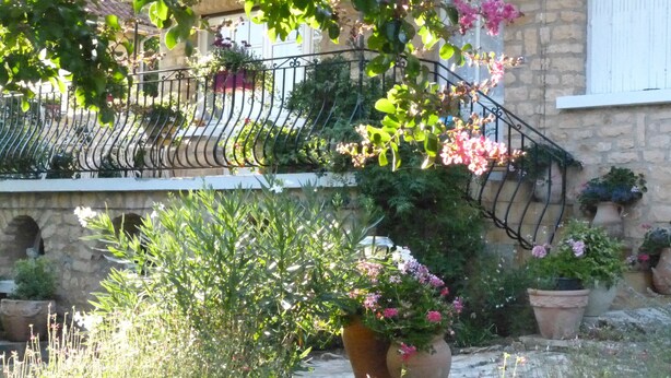 Un bâtiment en pierre doté d’un balcon, de plantes en pot et d’une balustrade en fer forgé.