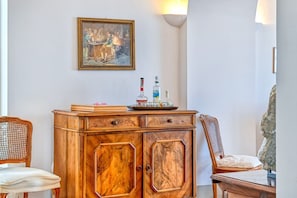 Un meuble en bois avec des tiroirs, une chaise en osier, un fauteuil rembourré et un tableau accroché au mur.