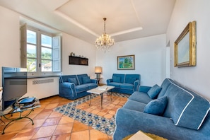 A living room with two blue sofas, a coffee table, a chandelier, and a patterned rug.