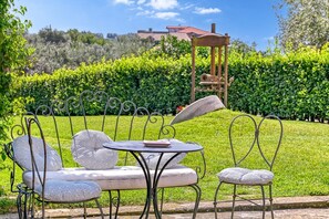 Une terrasse de jardin avec une table et des chaises en métal, entourée d’une végétation luxuriante et sous un ciel dégagé.