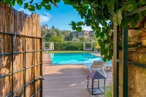Eine Holzterrasse mit Schwimmbecken, Liegestühlen und einer Pergola.
