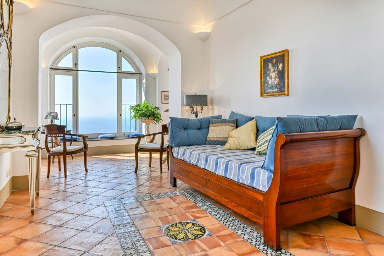 A spacious living room with a large window, a wooden sofa, a dining table with chairs, and a tiled floor.