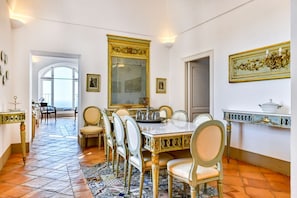 A dining area with a white table, gold chairs, and a large mirror.