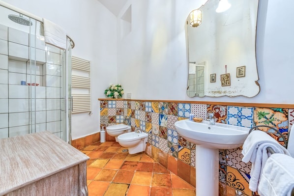 A bathroom with a shower, two toilets, a sink, and a tiled backsplash.