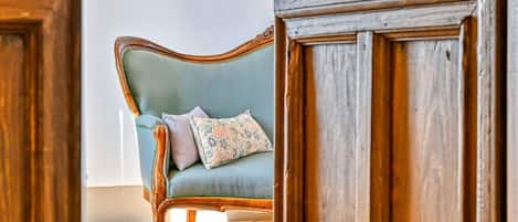 A room with a wooden door frame, a light blue sofa with floral cushions, and a tiled floor.