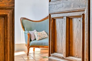 Une pièce avec un cadre de porte en bois, un canapé bleu clair orné de coussins à motifs floraux et un sol carrelé.