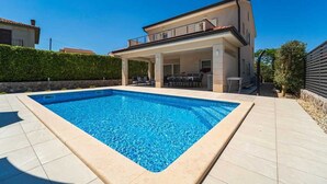 Ein modernes, zweistöckiges Haus mit Swimmingpool, Sitzgelegenheiten im Freien und einer überdachten Terrasse.