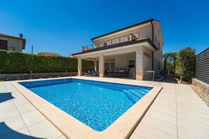 Une maison moderne à deux étages dotée d’une piscine, d’un espace salon extérieur et d’un patio couvert.