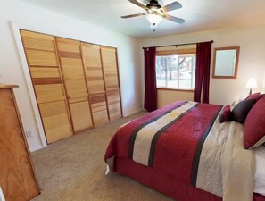 Une chambre à coucher avec un lit, un ventilateur de plafond, une fenêtre avec des rideaux et une armoire.