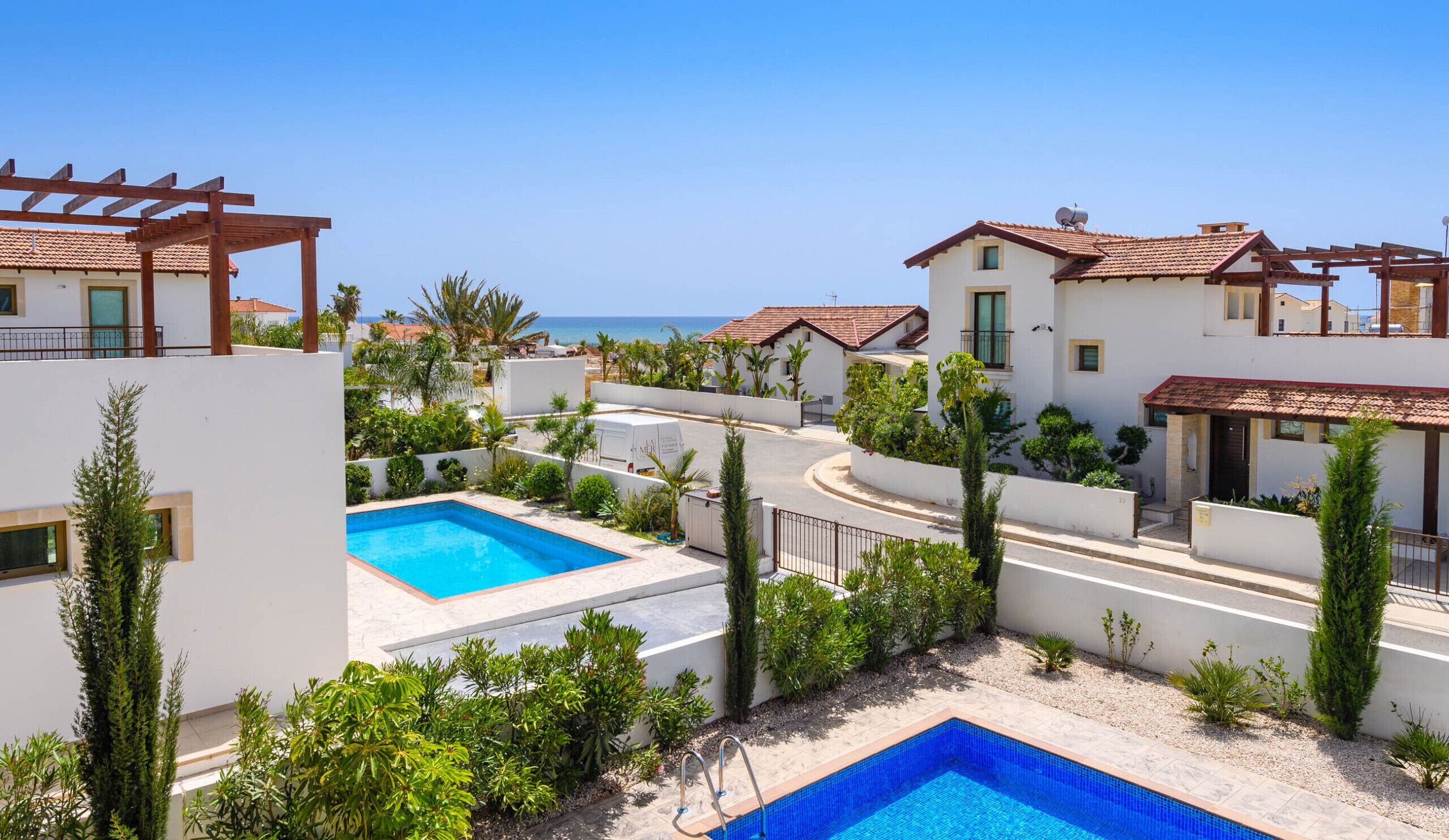 A residential area with two swimming pools, white buildings, and a view of the sea.