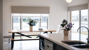 A modern kitchen with a dining area, large windows, and a view of the outside. - Waterfront Grand Villa in Sanctuary Lakes (Point Cook)