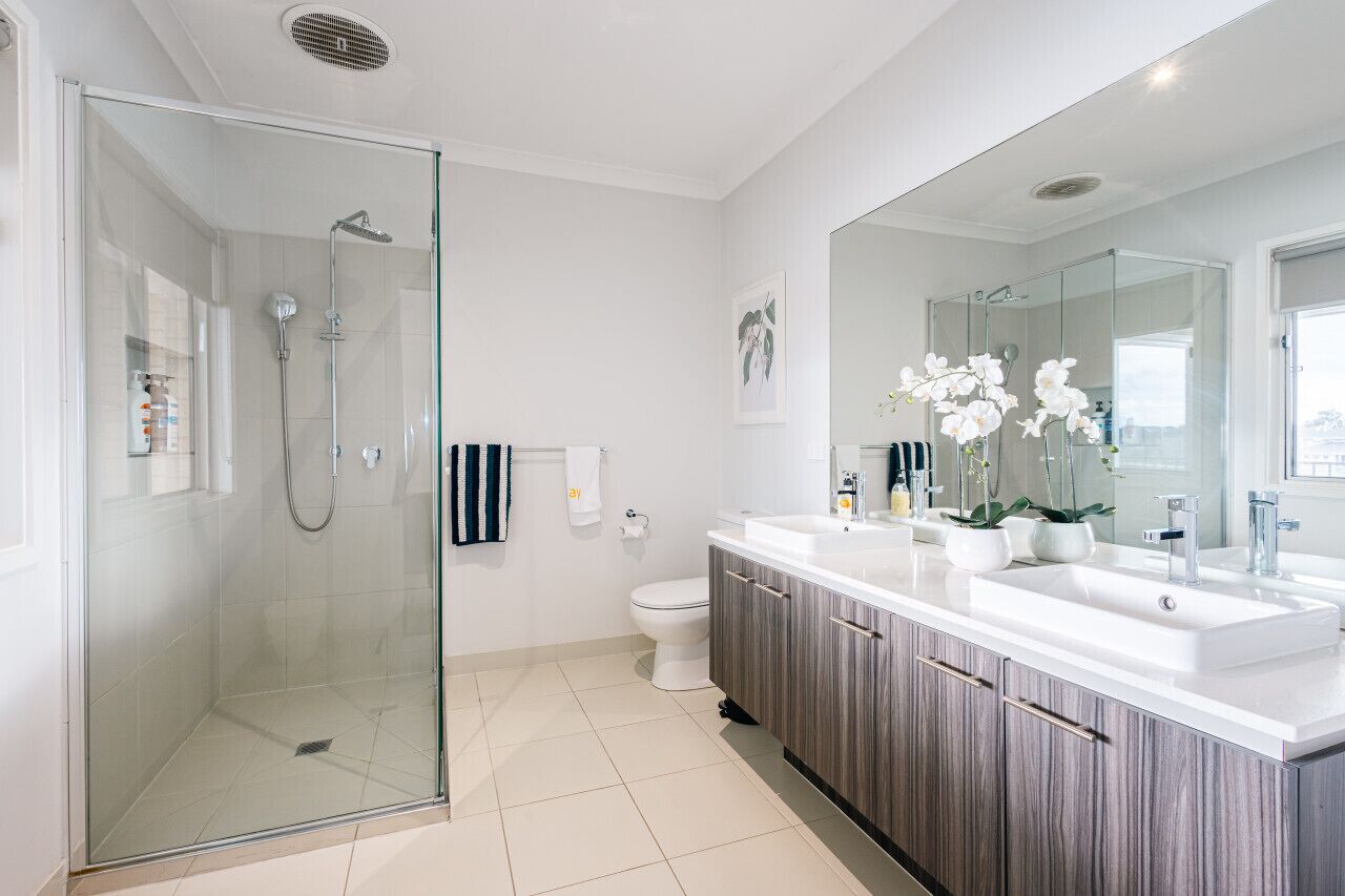 A modern bathroom with a glass-enclosed shower, a white toilet, and a vanity with a large mirror and sink.