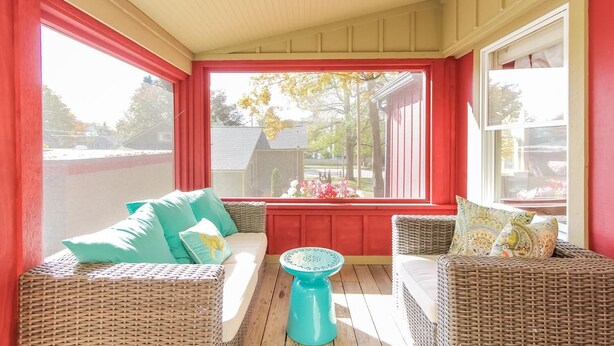A covered porch with wicker furniture and a blue table, overlooking a residential area. - The Oriole, hot tub, walk or Bike to Saugatuck! (Saugatuck)