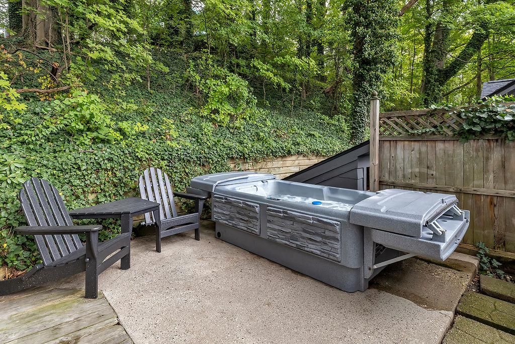 Una vasca idromassaggio con un pontile in legno e poltrone Adirondack in un rigoglioso giardino.