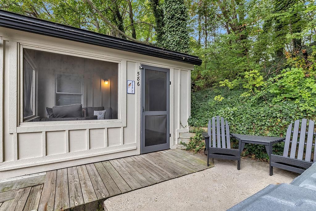 A cabin with a large window, a door, and a deck area with two Adirondack chairs.