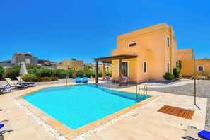 A swimming pool with lounge chairs and a covered seating area, surrounded by a building with a yellow facade.