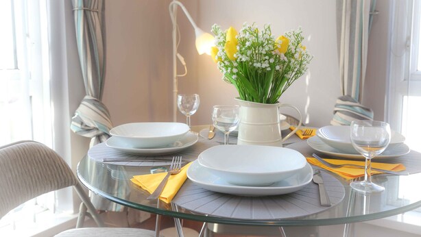 Ein Esstisch mit Geschirr, Besteck und einer Blumenvase.