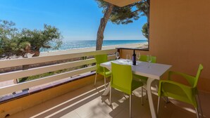 A balcony with a table and chairs, overlooking a beach.