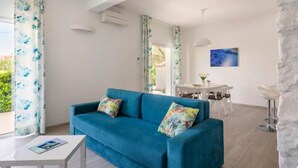 A modern living room with a blue sofa, a white coffee table, and a dining area with a white table and chairs. - Luxury family-friendly apartment with private pool, 10 min drive to center Split (Solin)