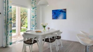 A dining area with a white table, four chairs with cushions, a vase with flowers, and a painting on the wall. - Luxury family-friendly apartment with private pool, 10 min drive to center Split (Solin)